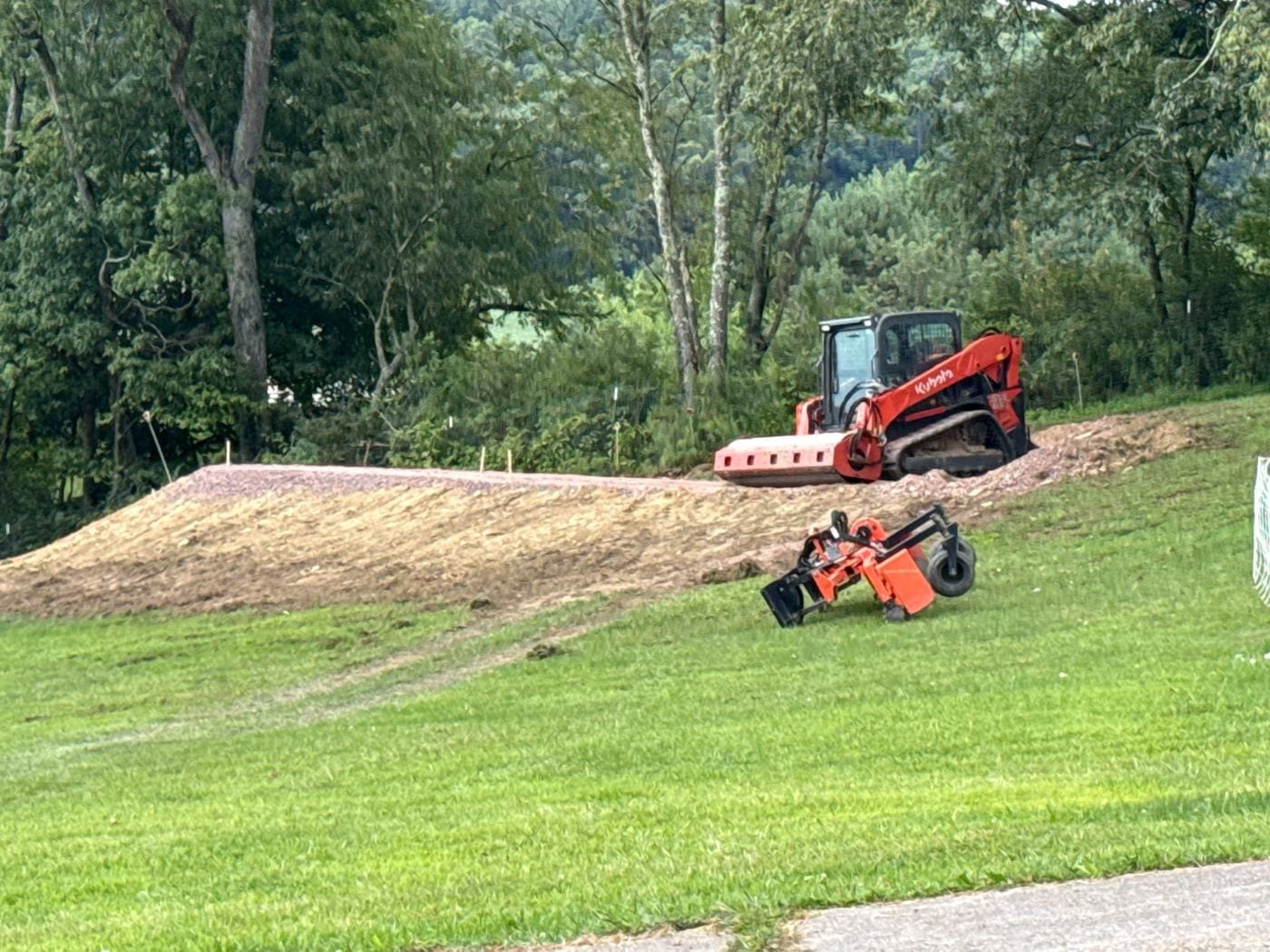 A track loader working the top of a fresh slope beside the lawn.