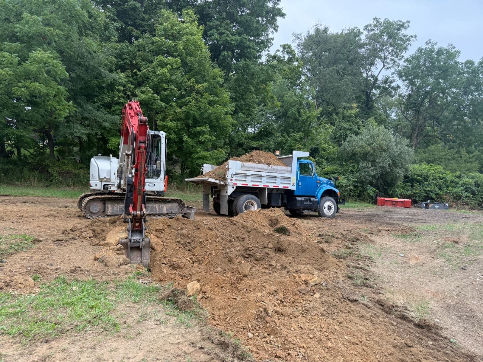 An excavator digging with a dump truck standing by.