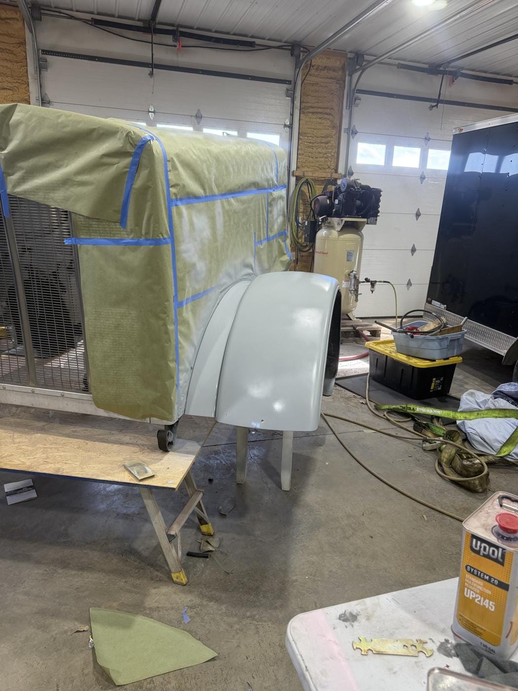A truck cab masked off in the shop, with a fender set beside it.