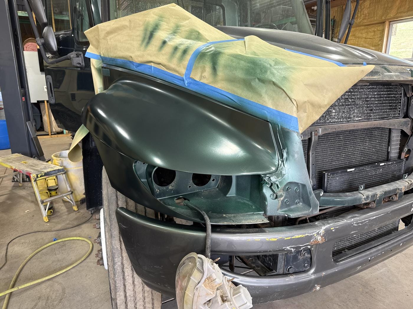 A green pickup front end, masked off around a fresh-painted fender.