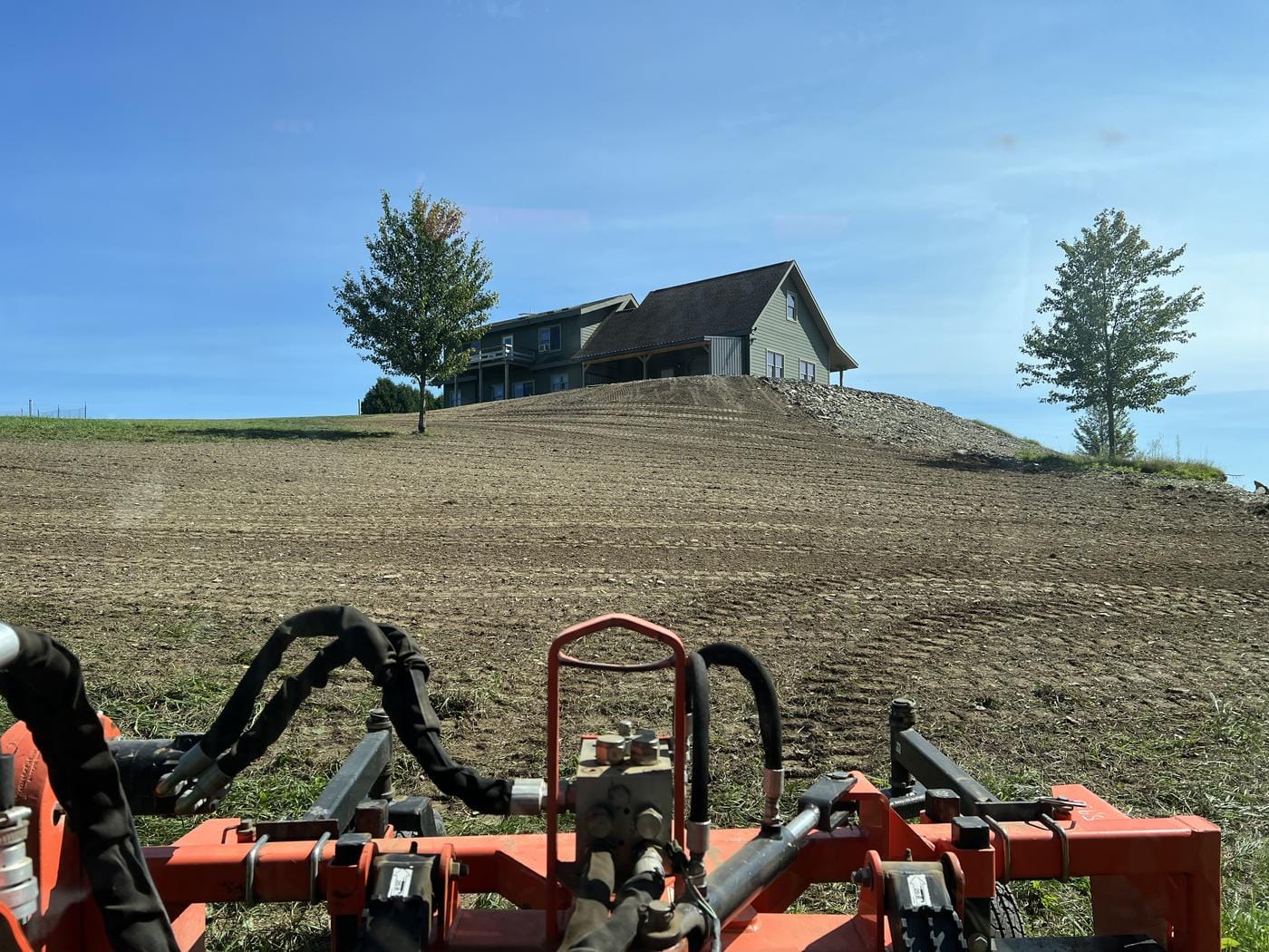 A fresh-graded hillside below a house, seen from the tractor.