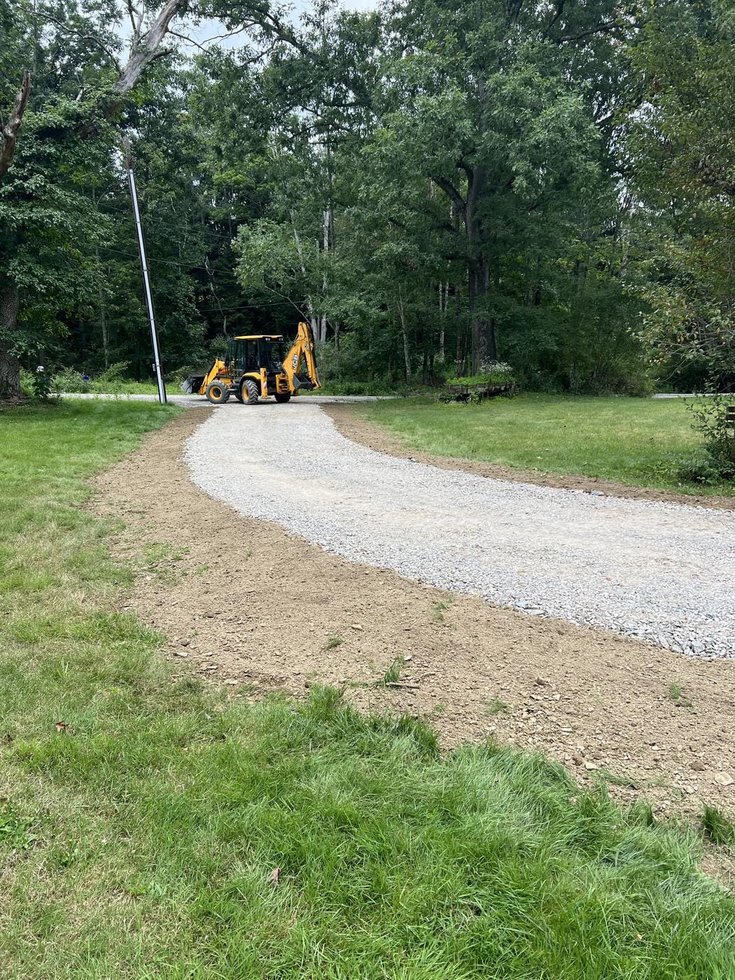 A new gravel drive curving through the lawn, with the backhoe at the top.