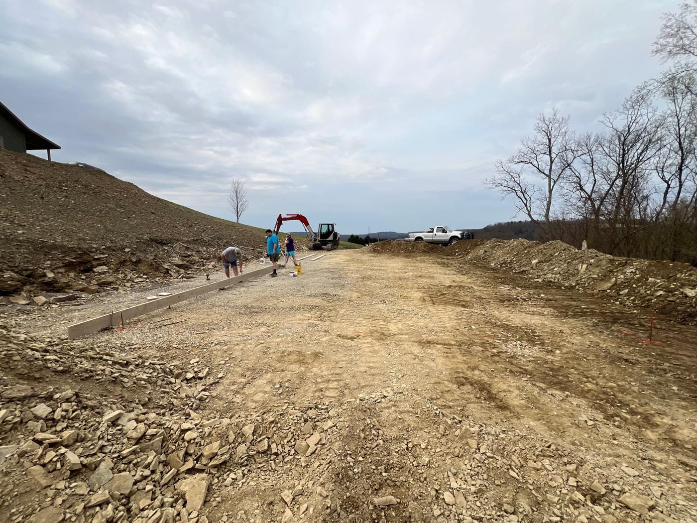 A crew on a rough-graded site, with the excavator at the far end.