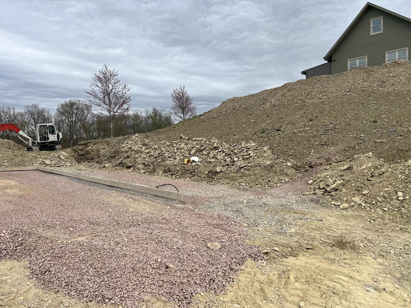 A stone pad below a fresh-cut bank, with the house up top.